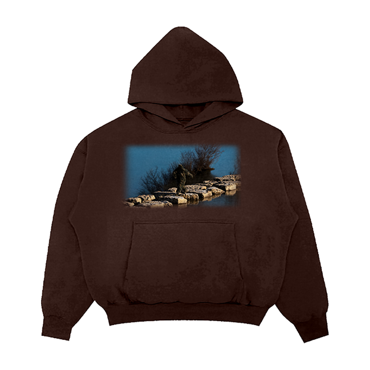 Brown hoodie with a scenic print on a nature-themed design of a Sasquatch waking on rocks in between a lake.