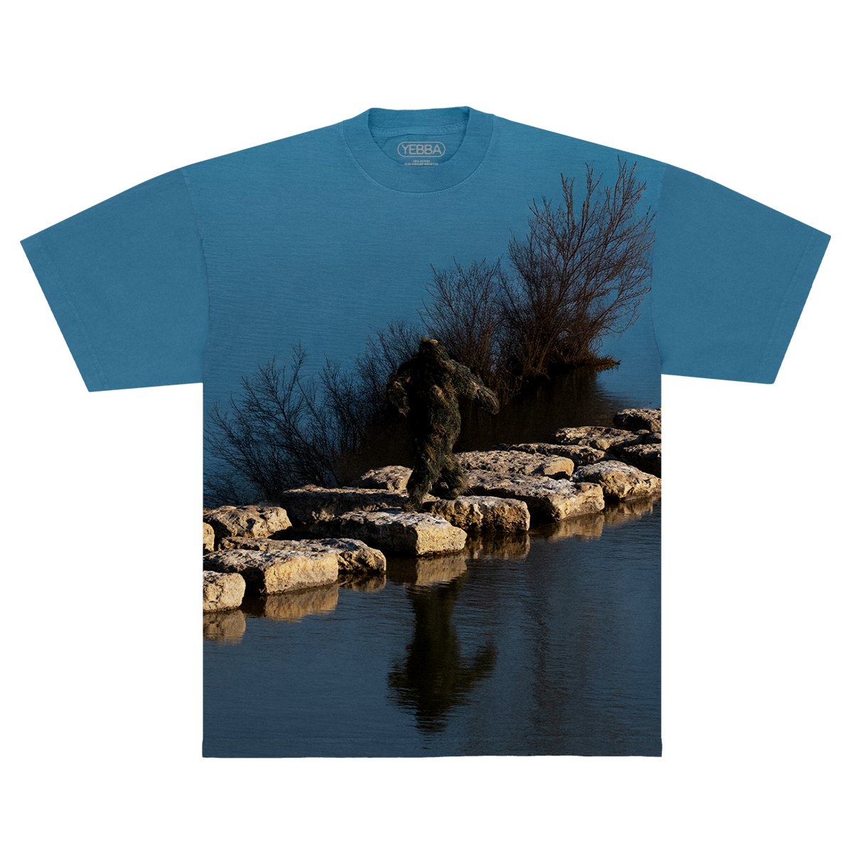 Blue shirt with a nature-themed design of a Sasquatch waking on rocks in between a lake on a blue background
